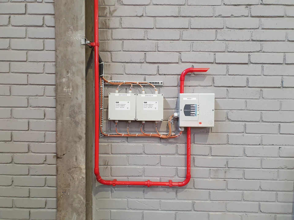 Détecteur de fumée VESDA, réseau de tubes rouges d’aspiration et modules raccordés sur un mur industriel